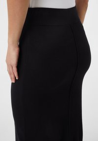 Jupe noire cintrée avec une texture lisse, dotée d'une large taille et de détails de couture. L'image montre la vue de dos, mettant en avant la silhouette.