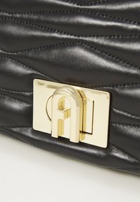 Borsa in pelle nera trapuntata con un'evidente chiusura in metallo dorato e logo impresso, che mette in risalto la sua finitura testurizzata.