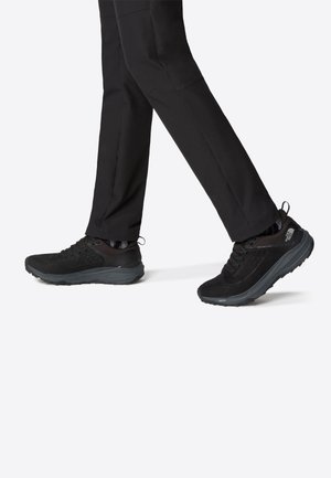 Zapatillas deportivas negras con parte superior de malla y sintético, cuello acolchado, cordones y suela de goma. Adecuadas para uso casual y actividades al aire libre.