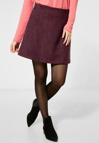 Kort, utsvängd kjol i strukturerad mörkrosa tyg med ett geometriskt mönster, kombinerad med svarta strumpbyxor och ankelskor.