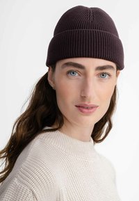 Knit beanie in dark burgundy, featuring ribbed texture and a central seam. Paired with a light beige textured sweater.