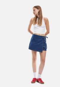 Denim wrap-hame, jossa on sidontadetail, keskisininen väri ja teksturoitu pinta. Yhdistetty valkoiseen cropped-toppiin ja punaisiin tennareihin.