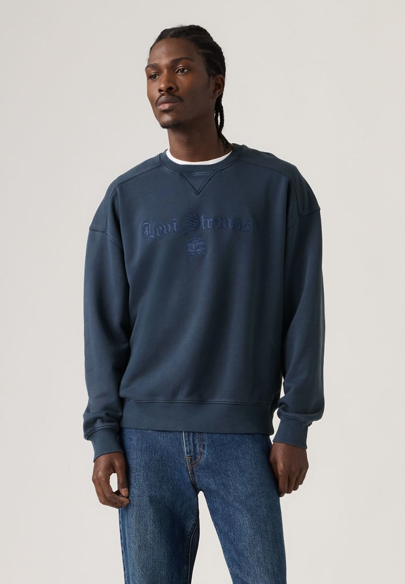 Felpa blu navy con scollo rotondo, logo "Levi Strauss" ricamato e polsini a costine, abbinata a jeans di denim blu.
