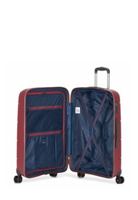 Red hard-shell suitcase with a textured surface, silver zipper, and four black wheels. Interior features navy fabric with compartments and straps.