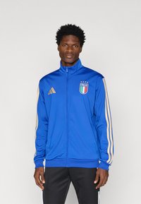 Μπλε αθλητικό τζάκετ από λείο ύφασμα με πλήρη φερμουάρ, χρυσές ρίγες στα μανίκια και έμβλημα της Ιταλίας με αστέρια.