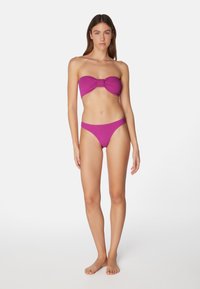 Lila bandeau-bikini med knutdetalj fram. Ribbtextur, matchande högmidjade botten, minimal täckning, inga dekorationer.
