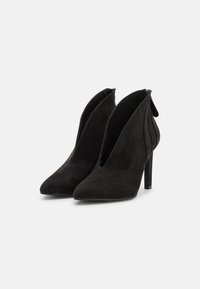 Botines de ante negros con puntera puntiaguda, diseño de frente partido y tacón de stiletto delgado. Incluye una cremallera trasera y una textura suave.