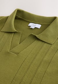Polo en maille vert olive avec des rayures verticales texturées et une étiquette de marque blanche indiquant « NEXT Regular Fit » à l’intérieur du col.