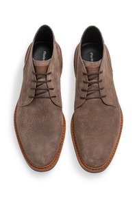 Zapatos de vestir de ante marrón con una textura suave, puntera redonda y detalles de cordones en marrón. Suela de goma natural con un borde en marrón claro contrastante.