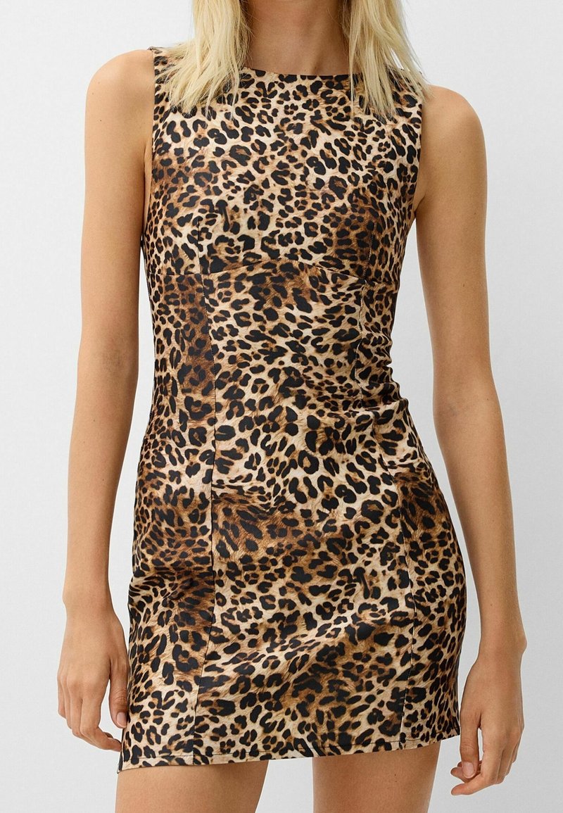 Robe mini sans manches et cintrée avec un motif léopard marron et noir portée par une personne debout.