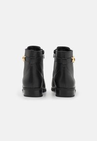 Bottines en cuir noir avec une finition texturée, dotées d'une boucle dorée en accent et d'un petit talon épais. Fermeture éclair sur le côté.