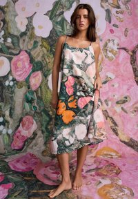 Kvetinové šaty s tenkými ramienkami, ktoré majú živý dizajn oranžového vtáka na zmiešanom vzore ružových a zelených kvetov na zodpovedajúcom pozadí.