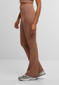 Bruine flare yoga broek van elastische stof, met een hoge taille en zijnaad, gecombineerd met grijze sportschoenen. Soepele textuur.