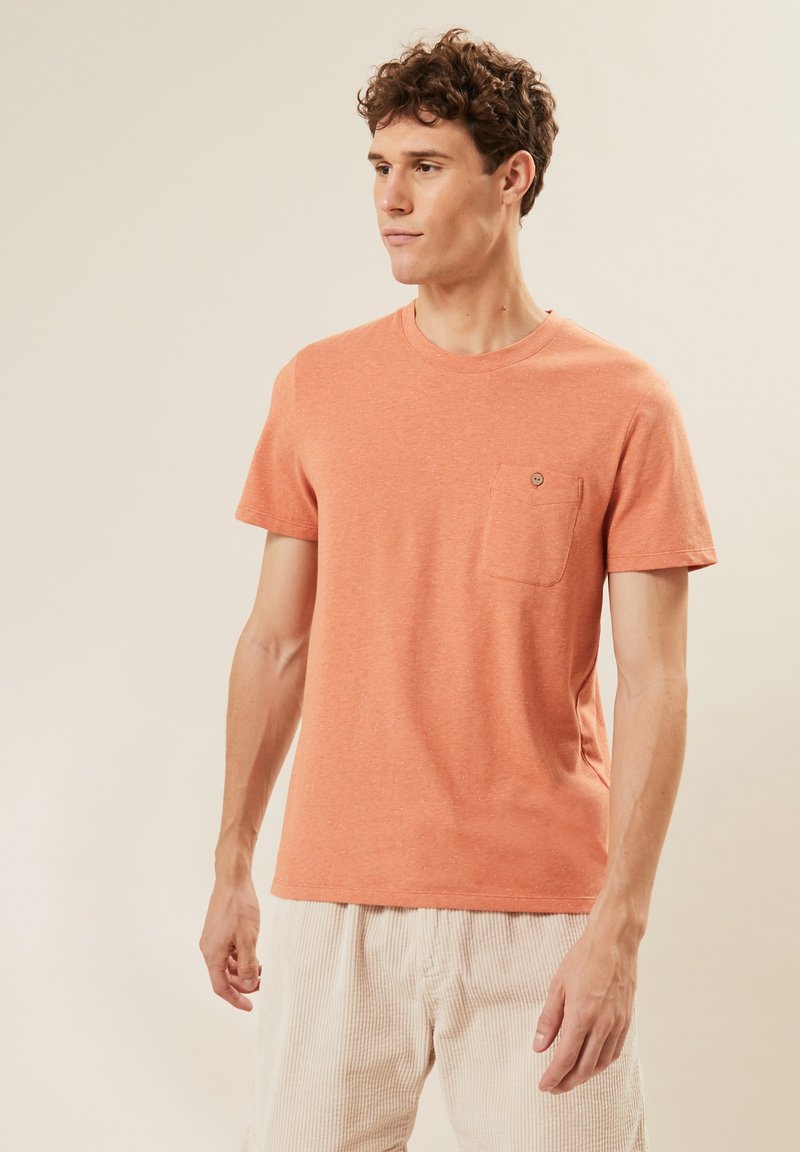 Orange Baumwoll-T-Shirt mit Rundhals, kurzen Ärmeln und einer Brusttasche. Hat eine strukturiert Oberfläche und ein dezentes Melange-Muster.