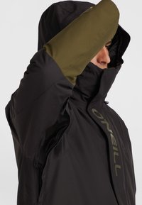 Veste d'extérieur noire avec des manches vert olive, col haut, capuche et fermeture éclair frontale. Présente le logo O'Neill et des panneaux latéraux en mesh.