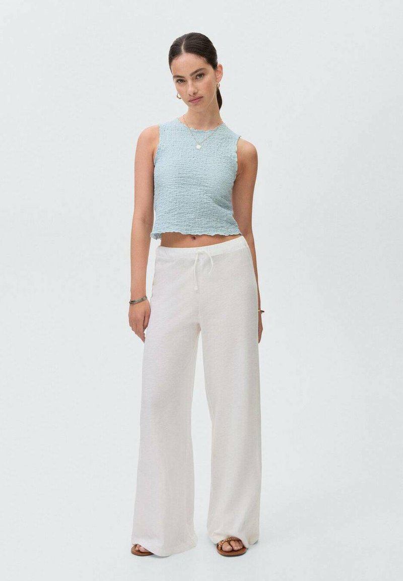 Svetlomodrý crop top s textúrovanou látkou a ryhovanými okrajmi, skombinovaný s voľnými bielymi širokými nohavicami a hnedými sandálmi.