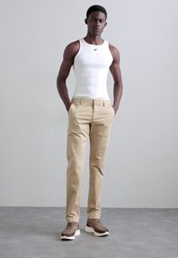 Hvid tanktop, beige bukser og brune sneakers. Casual outfit med en figursyet design. Bukserne har lommer; sneakersne har et struktureret mønster.