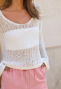 Pull blanc en tricot avec un motif à mailles ajourées, manches longues et encolure arrondie, associé à un short à rayures roses avec cordon de serrage.