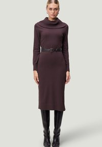 Braunes Strickkleid mit einem Schalkragen, langen Ärmeln und einem Taillengürtel. Verfügt über eine gerade Silhouette und ein geripptes Muster. Schwarze kniehohe Stiefel.