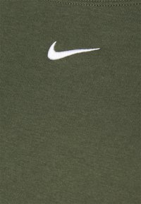 Olivgrön textil med en närbild av en ribbad design och en vit Nike-logotyp. Slät struktur med synliga sömmar.