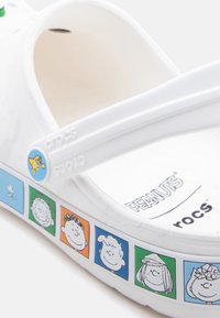 Λευκή σαγιονάρα Crocs με πρόσωπα χαρακτήρων από το κόμικ Peanuts σε έγχρωμα τετράγωνα κατά μήκος της σόλας και κρεμαστό Snoopy στο λουράκι.