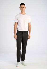 Zwarte slim-fit broek met een gladde textuur, gecombineerd met een effen wit t-shirt en witte sneakers. Eenvoudig ontwerp, zonder patronen of accenten.