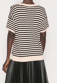 Persoon met een beige en zwarte gestreepte shirt met korte mouwen, gecombineerd met een zwarte geplooide rok, gezien van achteren.