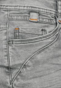 Jeans in denim grigio con finitura sbiadita. Presentano dettagli in cucitura arancione, un piccolo taschino anteriore e design standard per le tasche posteriori.