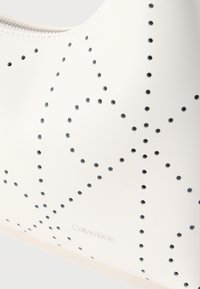 Λευκή δερμάτινη τσάντα με διάτρητο σχέδιο αστεριού και διακριτικό λογότυπο Calvin Klein, κοντινή όψη της υφής και των ραφών.