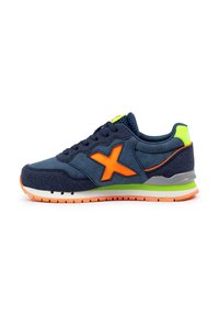 Zapatillas deportivas azul marino con detalles en naranja, parte superior texturizada y suela verde y gris, con un logotipo destacado en el lateral y cordones.