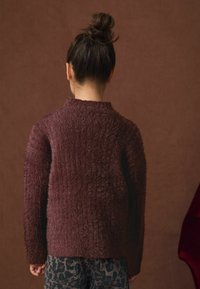 Burgundy fluffig tröja med hög krage, texturerad yta och långa ärmar, kombinerad med leopardmönstrade byxor. Bakvyn visas.