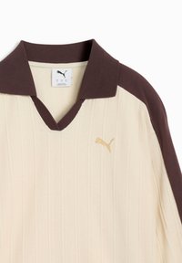Μπεζ ριγωτό πόλο μπλουζάκι με σκούρο καφέ γιακά και ρίγα στον ώμο, με μικρό χρυσό λογότυπο Puma στο αριστερό στήθος.