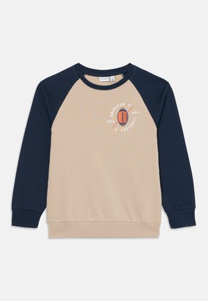 Felpa con maniche raglan beige e navy con la scritta "American Football ESTD 1999" e grafica di un pallone da football sul petto.