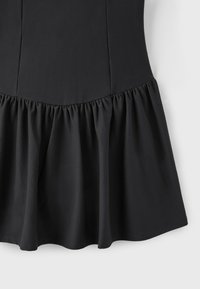 Section de robe noire montrant le haut ajusté et l'ourlet à volants froncés et évasés sur fond blanc.