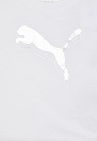 Valge T-särk, millel on peegeldava hõbedase Puma logos, kes hüppab, sile tekstuur ja ümmargune kaelus.