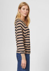 Beige und marine gestreifter Strickpullover mit V-Ausschnitt und langen Ärmeln, kombiniert mit blauen Jeans, die eine lockere Passform und gerippte Bündchen zeigen.