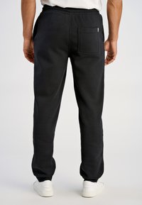 Zwarte joggingbroek met een comfortabele pasvorm, voorzien van een achterzak en een elastische tailleband. De stof lijkt zacht en heeft een textuur.