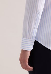 Jasnoniebieska i biała koszula w paski z mankietami na guziki. Na mankiecie mała czarna haftowana kwiatowa aplikacja. Gładka bawełniana tkanina.