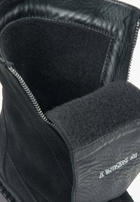 Zwarte suède enkellaars met een ritssluiting, zachte textielen voering en gladde leren accenten rond de opening en hak.