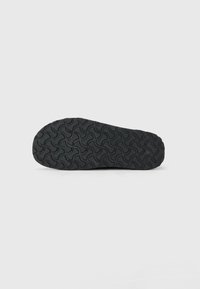 Black shoe sole with textured, wavy tread pattern designed for grip, displayed on a plain white background.