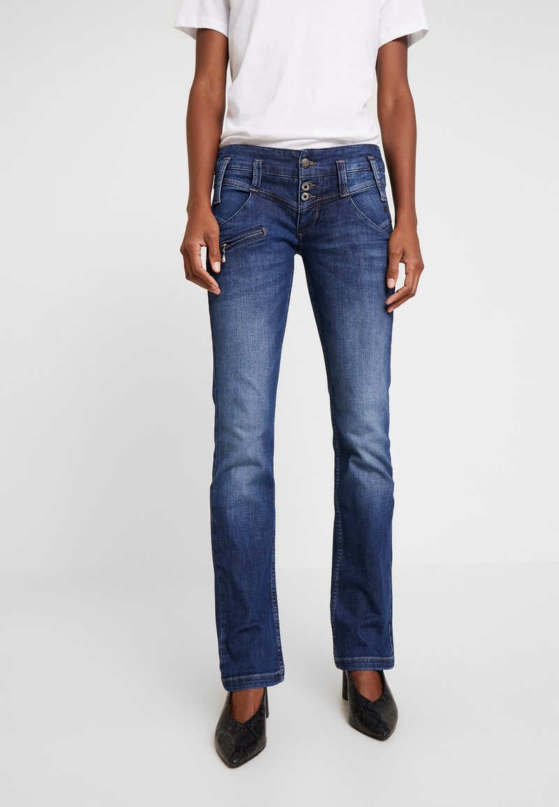 Siniset farkut, joissa on suora lahje, kevyesti haalistunut pinta, neljä taskua ja napillinen edessä. Yhdistetty mustien korkokenkien kanssa.