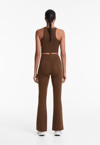 Brauner athletischer Crop-Top und ausgestellte Leggings aus dehnbarem Material, mit glatter Textur und minimalistischer Gestaltung, in passender Silhouette.