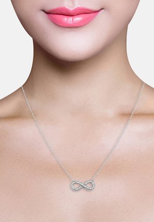Silbernes Unendlichkeitshalsband mit einer zarten Kette, das klare Edelsteine, die im Unendlichkeitssymbol eingearbeitet sind, zeigt und auf einem glatten Hautton hängt.