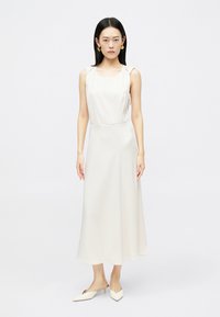 Σατέν μίντι φόρεμα σε κρεμ χρώμα, με τετράγωνη λαιμόκοψη, λεπτές τιράντες και ρέουσα σιλουέτα. Σε συνδυασμό με μυτερά μules.