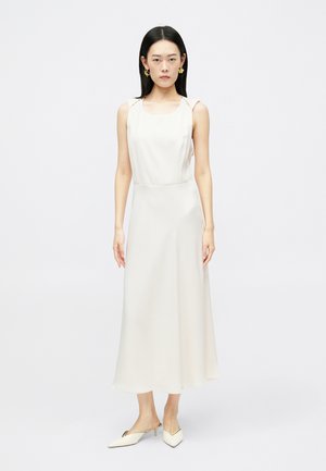 Krém színű, szatén midi ruha négyzet alakú nyakkivágással, vékony pántokkal és lebegő sziluettel. Hegyesorrú mules cipővel párosítva.