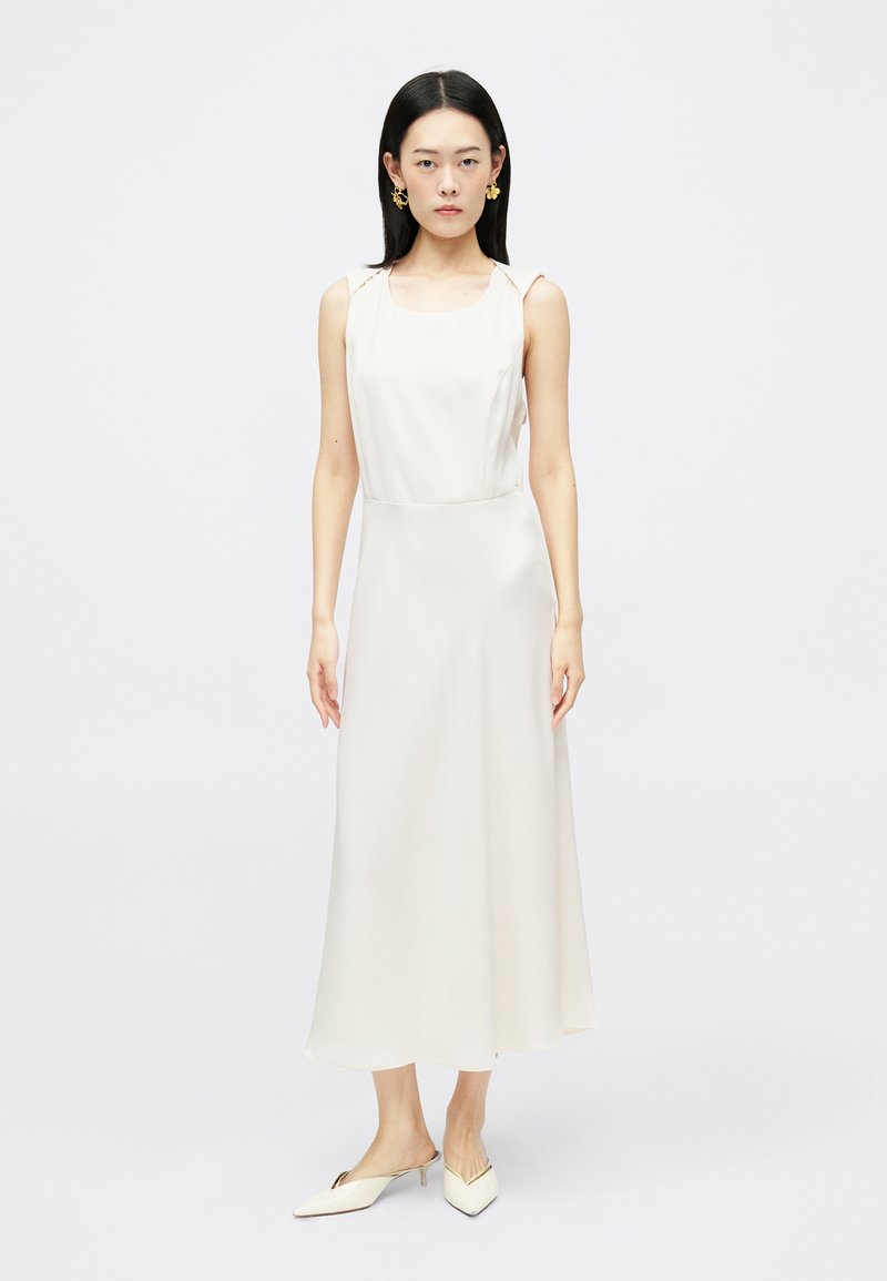 Σατέν μίντι φόρεμα σε κρεμ χρώμα, με τετράγωνη λαιμόκοψη, λεπτές τιράντες και ρέουσα σιλουέτα. Σε συνδυασμό με μυτερά μules.