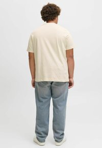 T-shirt en coton beige à manches courtes, coupe décontractée, associé à un jean en denim bleu clair et des baskets blanches.