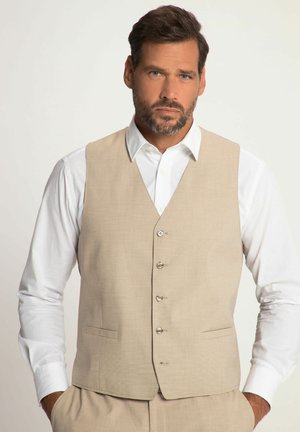 Chaleco beige con solapa muesca, bolsillos frontales y cinco botones. Lleva una camisa blanca debajo. Tejido suave con una sutil textura.