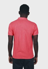 Rotes Poloshirt mit weicher Textur, kurzen Ärmeln und einem Kragen, das ein dezentes Melange-Muster und einen geraden Saum aufweist.