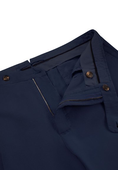 Granatowe spodnie z częściowo rozpiętym zamkiem błyskawicznym i zapięciem na guzik, ukazujące pas i szczegóły wewnętrznej tkaniny na białym tle.